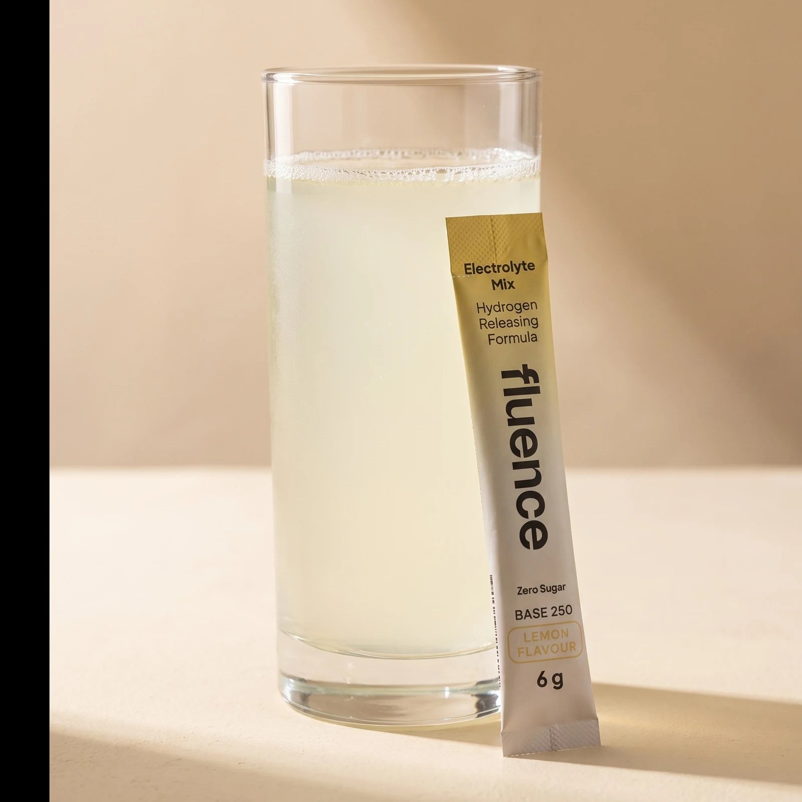A glass of Base 250 Lemon made up, beside a Lemon sachet