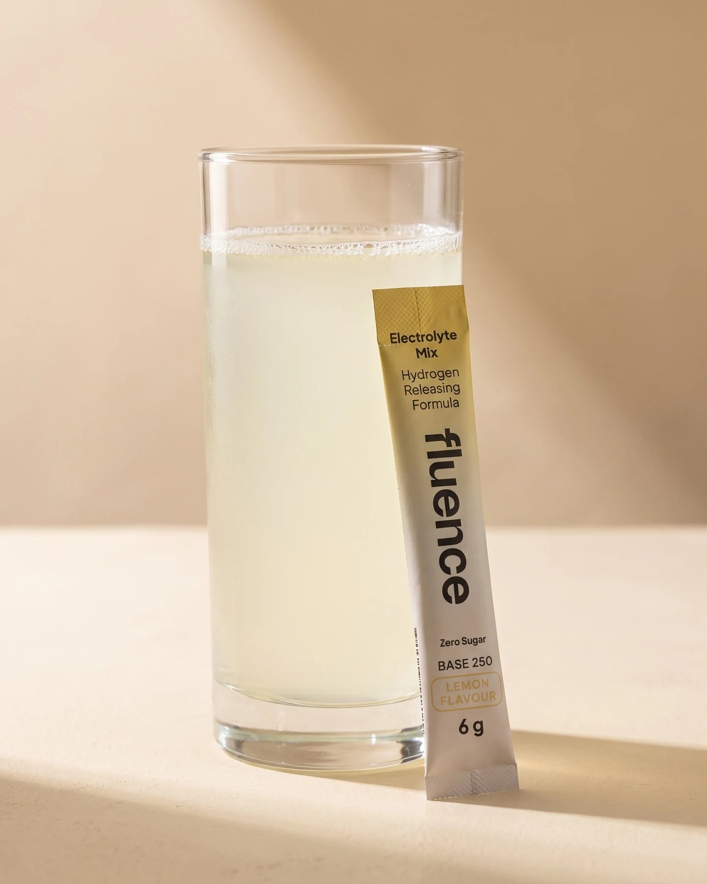 A glass of Base 250 Lemon made up, beside a Lemon sachet