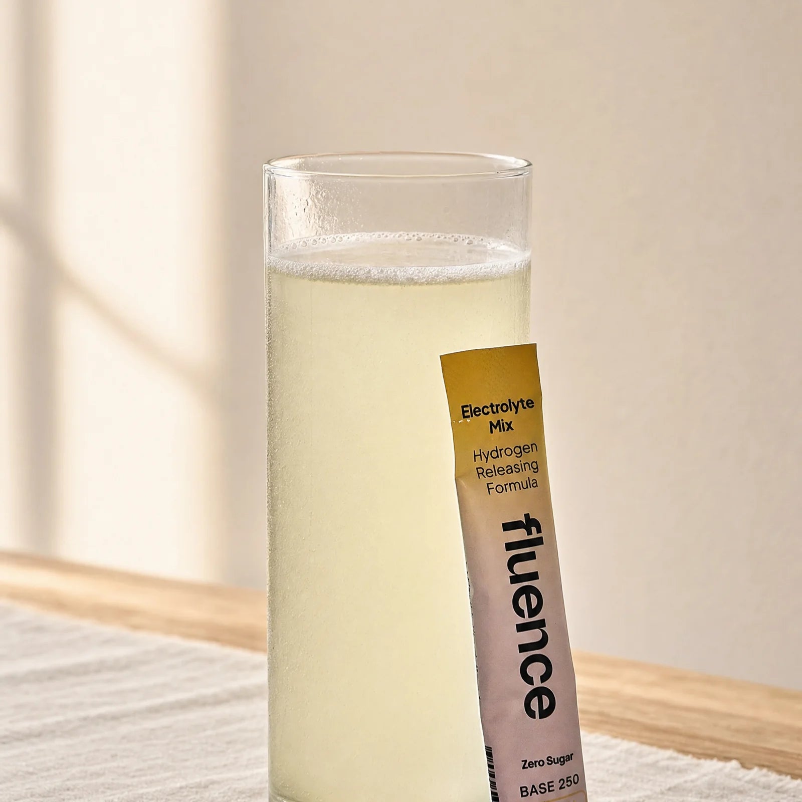 A glass of Base 250 beside a sachet, on an oak table