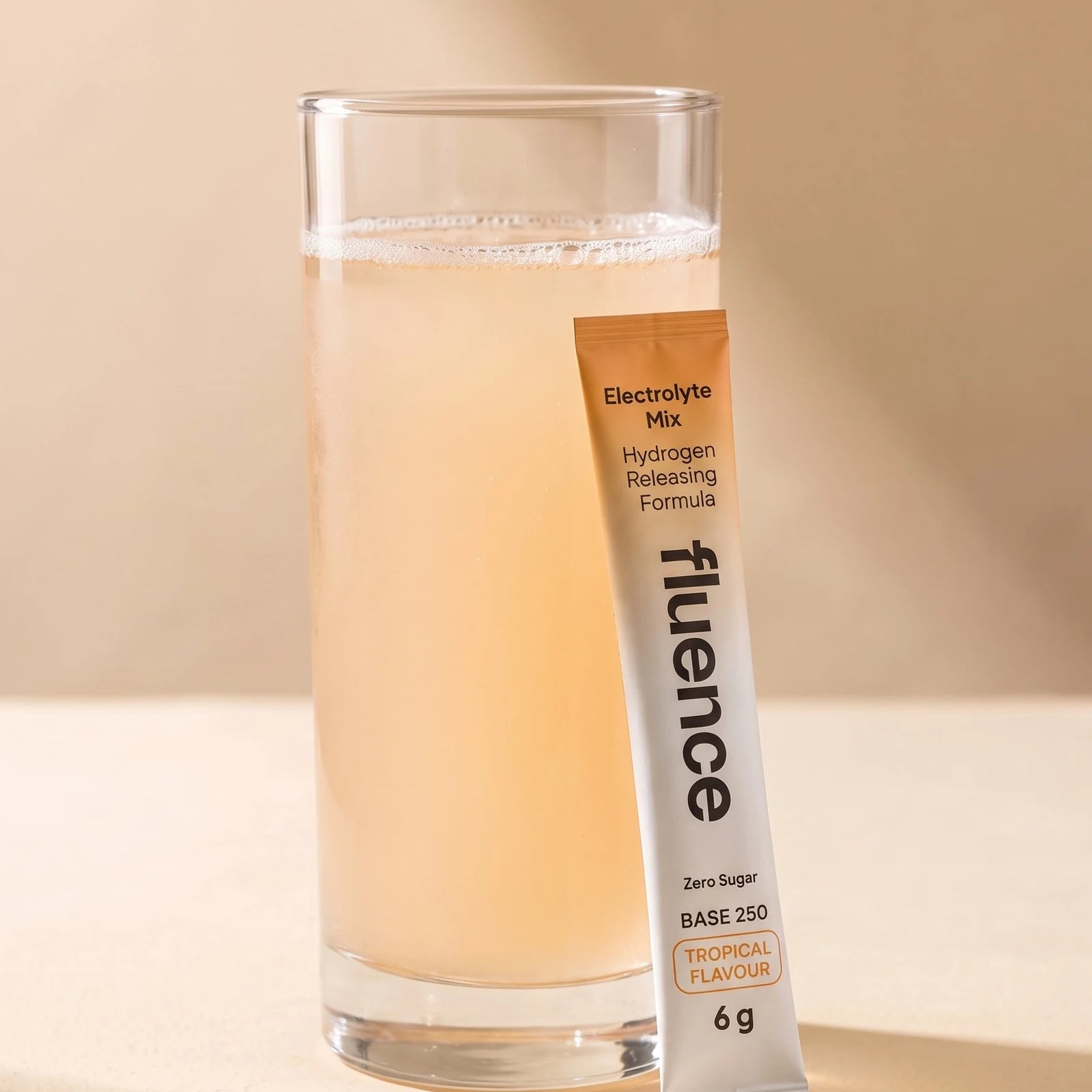 A glass of Base 250 Tropical made up, beside a Tropical sachet