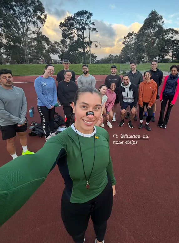A run club group on an athletics track, with the coach in front wearing a Fluence nasal strip