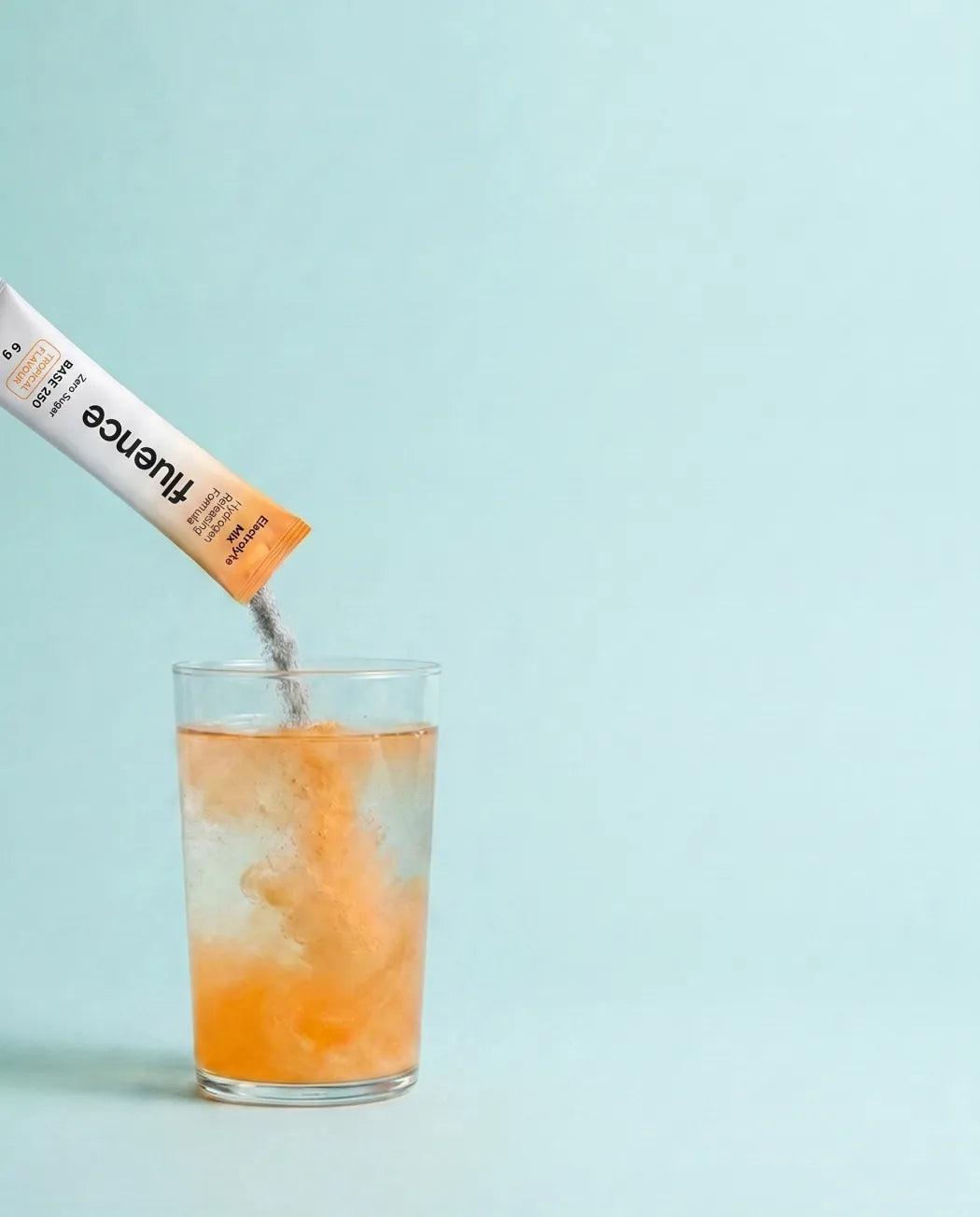 A Base 250 sachet stirred into a glass of water, fizzing as it dissolves